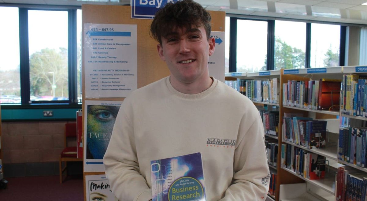 Male student holding a book in a library setting